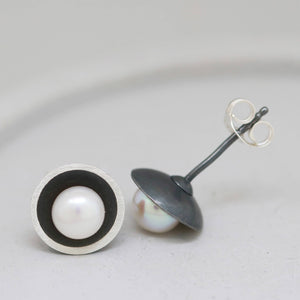 Single black pearl stud earring angled on grey dish to show polished silver rim around the oxidised dome