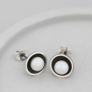 Close-up of modern black pearl stud earrings on grey dish highlighting the contrast between matte black silver and bright pearl