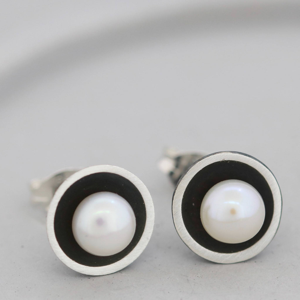Black pearl stud earrings on a grey dish showing the oxidised silver dome and central freshwater pearl