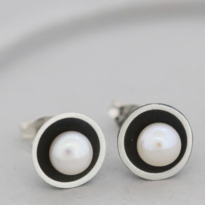 Black pearl stud earrings on a grey dish showing the oxidised silver dome and central freshwater pearl