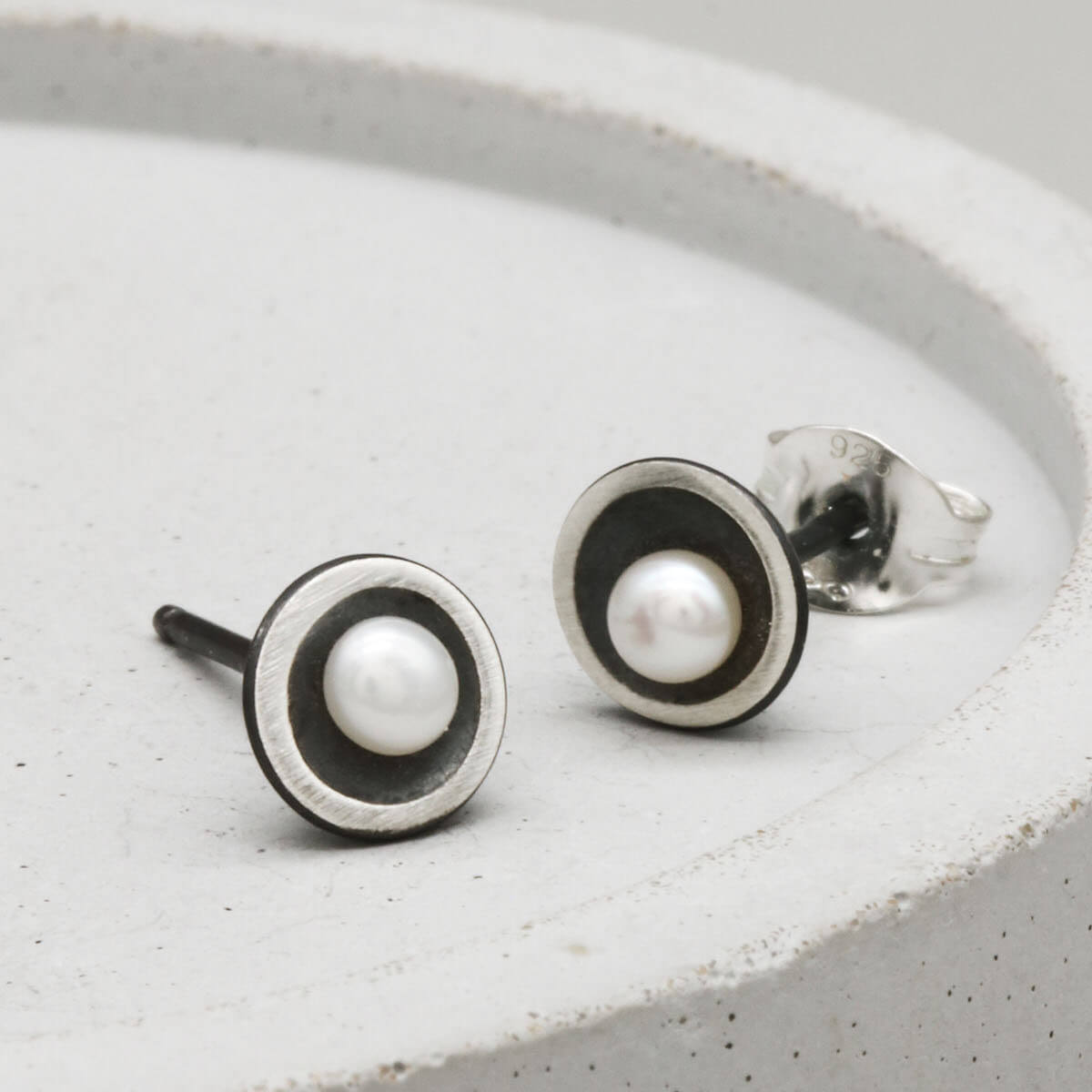 Small black pearl stud earrings in oxidised sterling silver with an elegant Art Deco-inspired domed design.