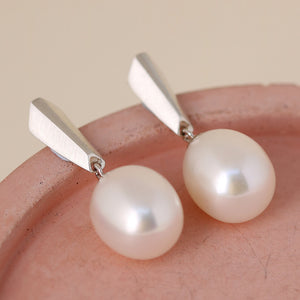 Flat-lay of silver dangle pearl earrings on a pink dish, ideal for brides seeking pearl drop earrings for wedding styling.