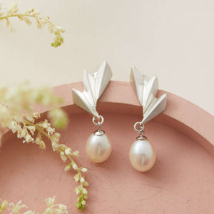 Earrings displayed on fabric to highlight shine and texture, sterling silver drop pearl earrings suited to bridal and evening wear.
