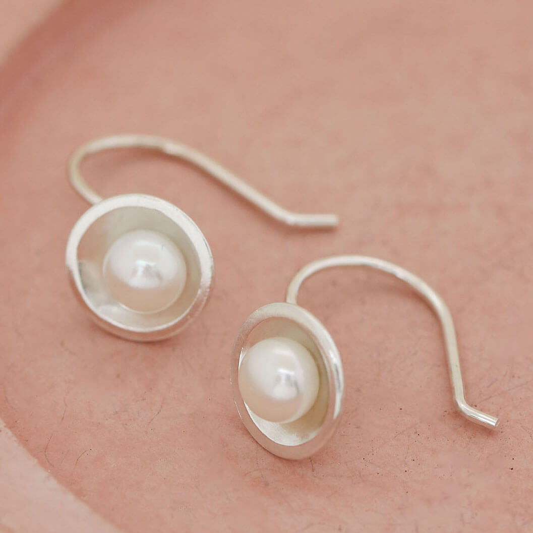 Handmade sterling silver drop freshwater pearl earrings with genuine freshwater pearls displayed on a soft pink ceramic dish, highlighting their elegant Art Deco-inspired design.