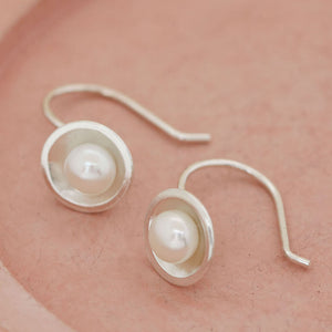 Handmade sterling silver drop freshwater pearl earrings with genuine freshwater pearls displayed on a soft pink ceramic dish, highlighting their elegant Art Deco-inspired design.