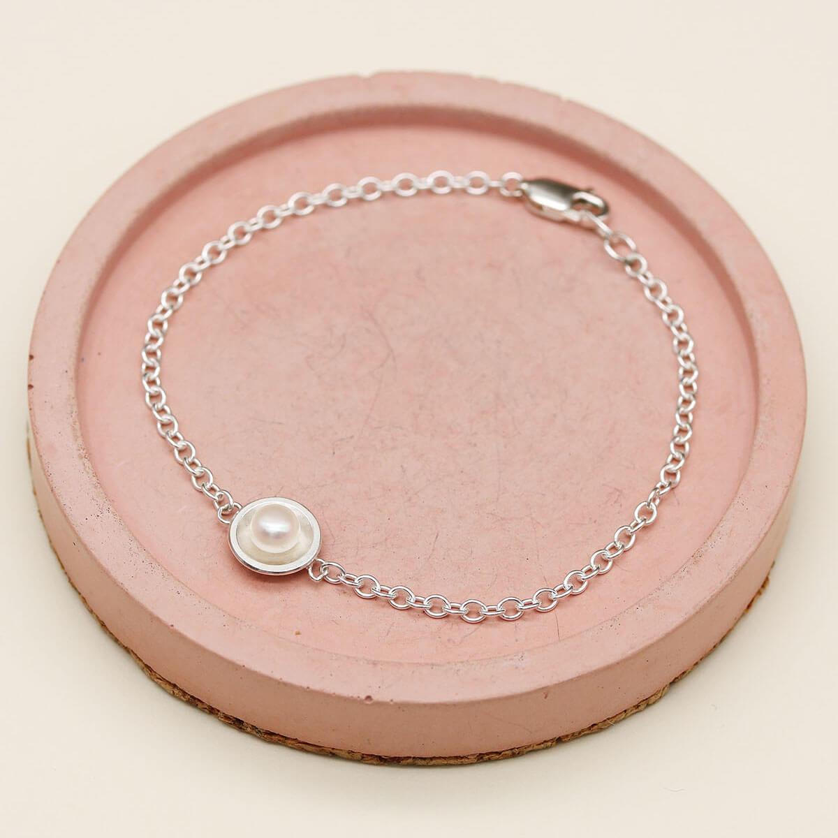 Delicate sterling silver and pearl bracelet displayed on a pink ceramic dish, highlighting the genuine freshwater pearl and fine chain.