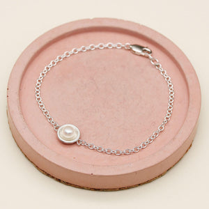 Delicate sterling silver and pearl bracelet displayed on a pink ceramic dish, highlighting the genuine freshwater pearl and fine chain.