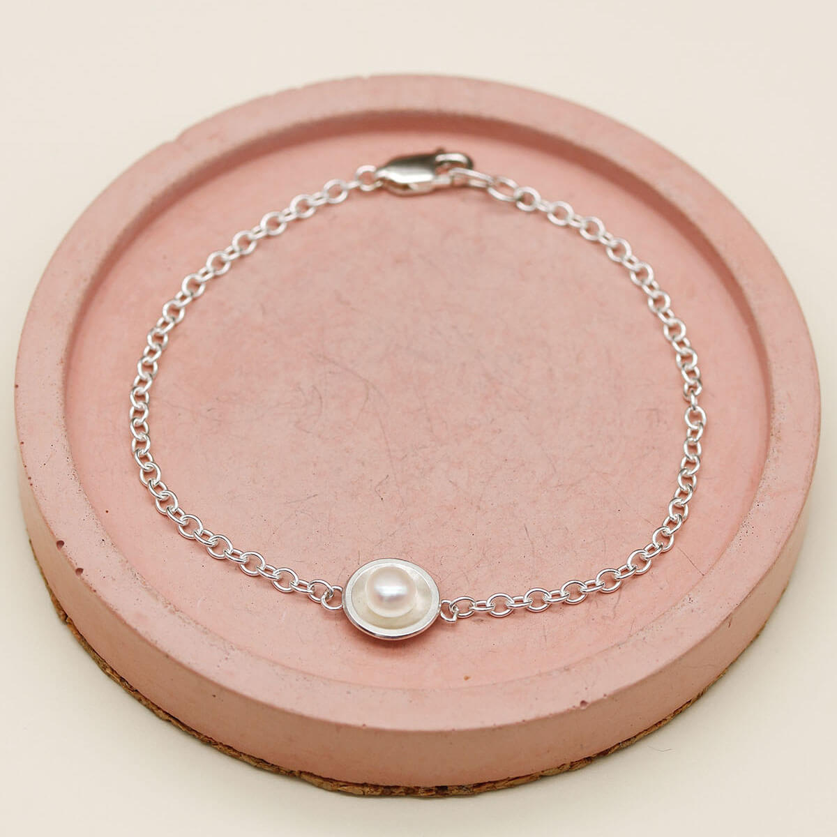 Handmade sterling silver pearl bracelet with a genuine freshwater pearl displayed on a pink ceramic dish.