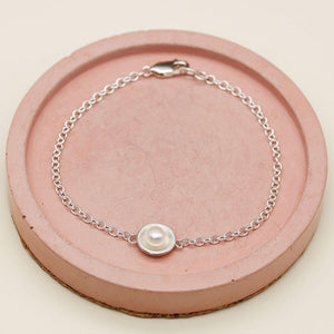 Handmade sterling silver pearl bracelet with a genuine freshwater pearl displayed on a pink ceramic dish.