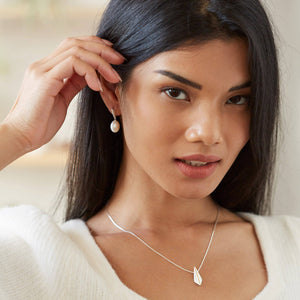 Close-up of the earrings worn, capturing the lustrous pearls and geometric silver detail in natural light.