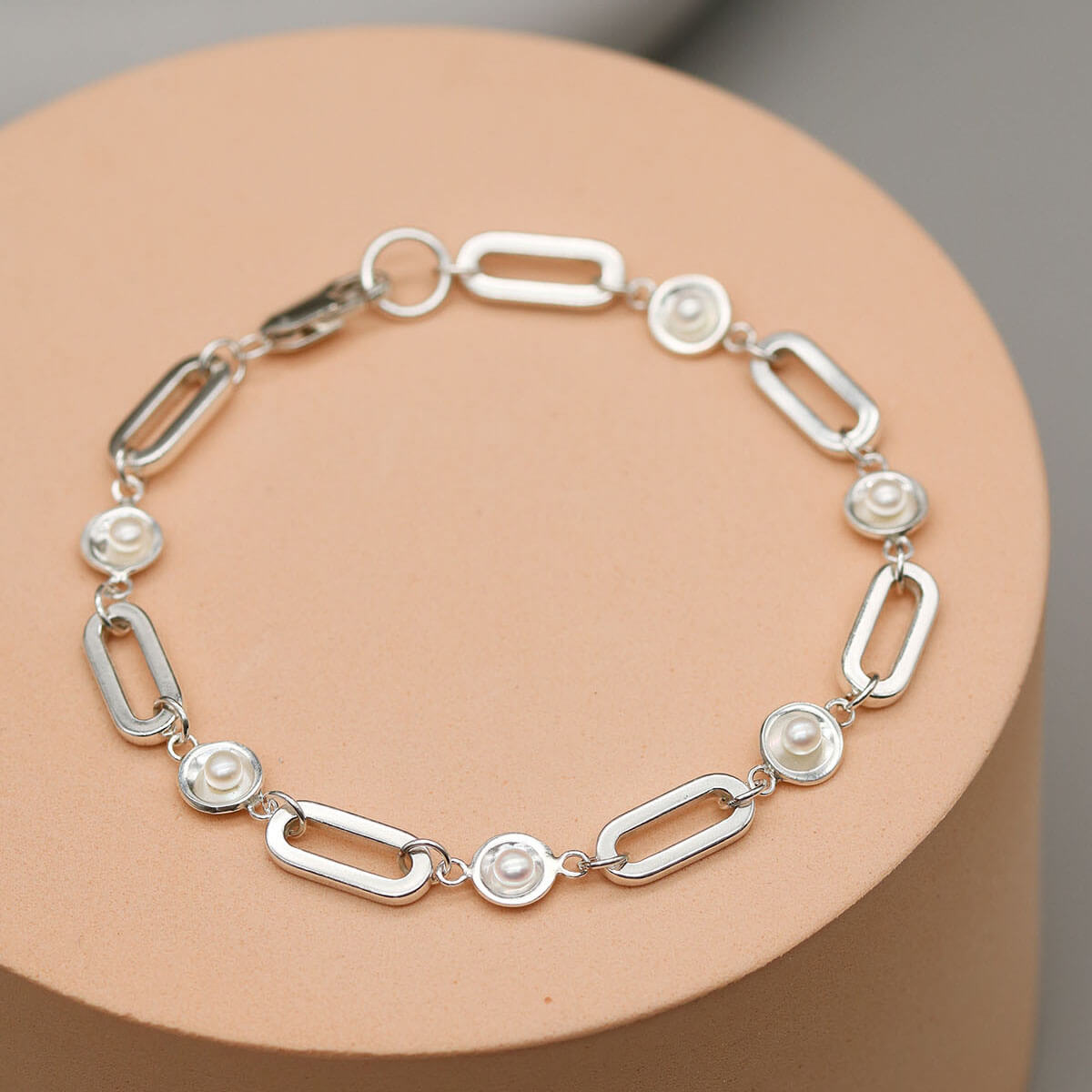Handmade sterling silver pearl chain bracelet featuring five genuine freshwater pearls on a bold rectangular sterling silver chain displayed on a pink plinth.
