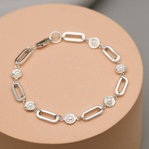 Handmade sterling silver pearl chain bracelet featuring five genuine freshwater pearls on a bold rectangular sterling silver chain displayed on a pink plinth.