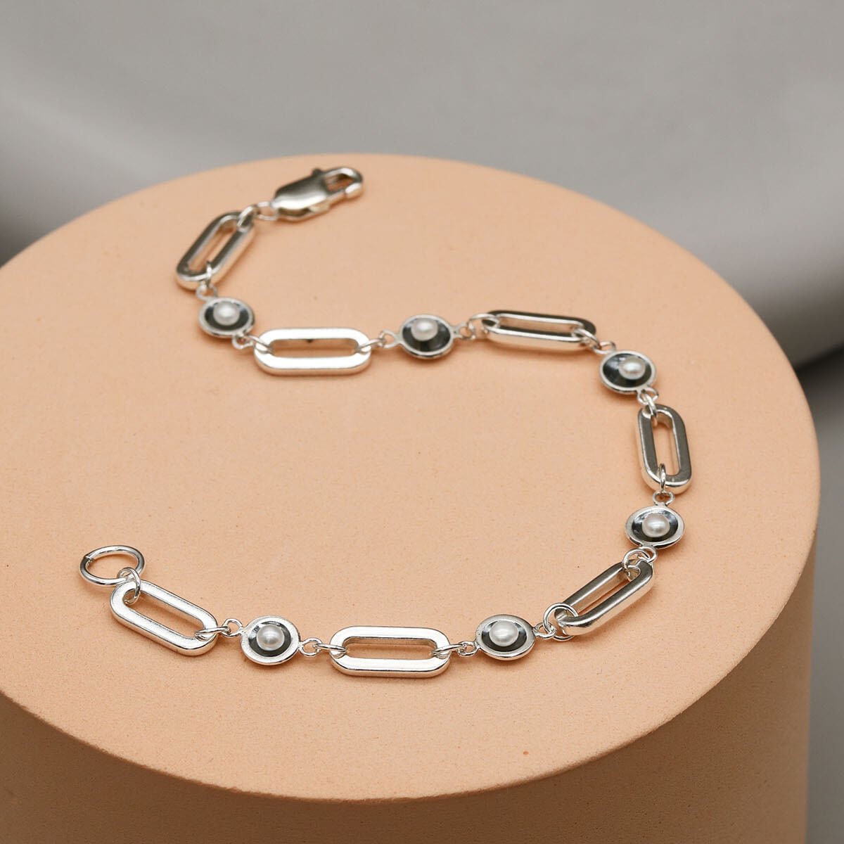 Contemporary black pearl chain bracelet displayed on a pink pedestal, showcasing handcrafted sterling silver links and freshwater pearls.