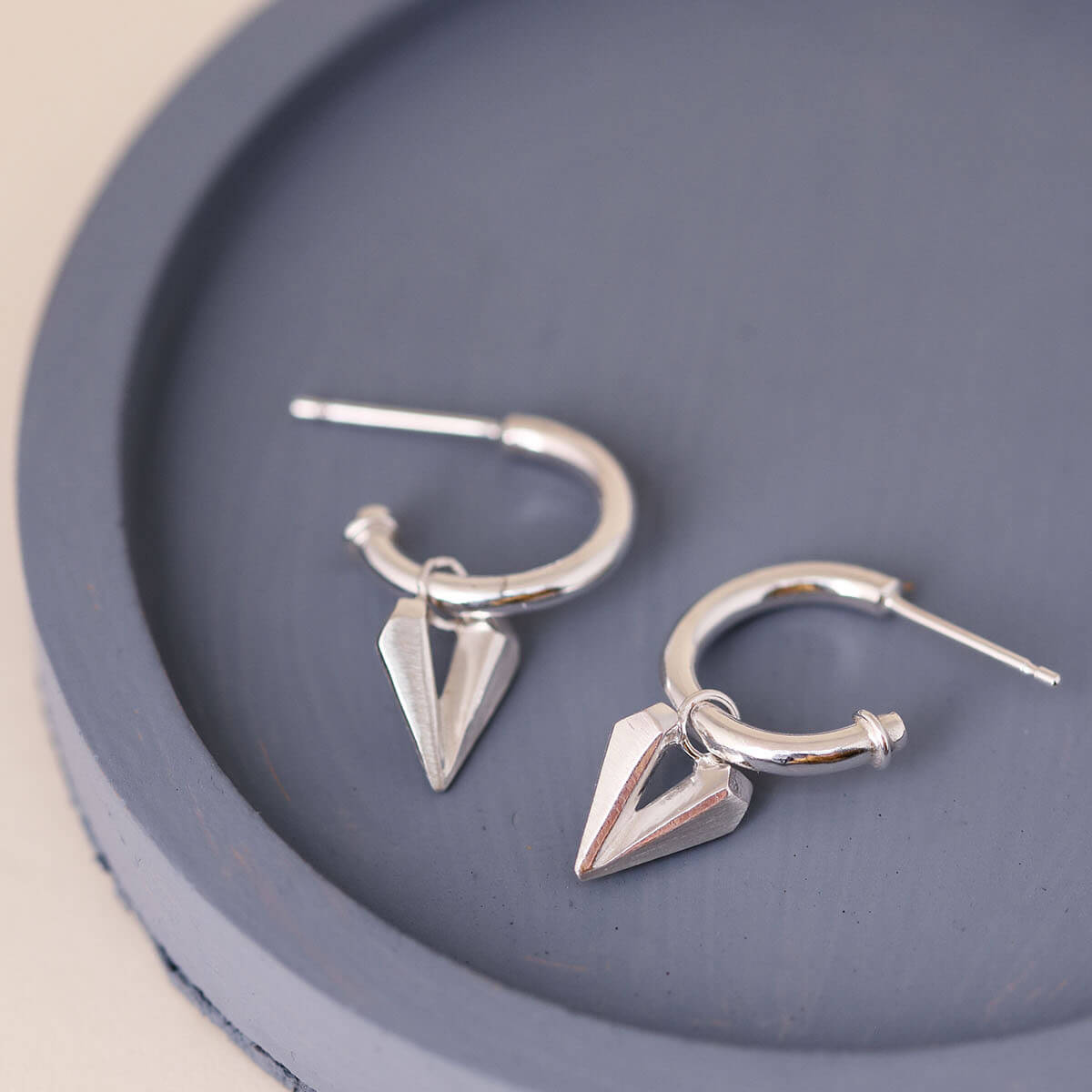 Silver hoop earrings with heart charm displayed on a blue dish, sterling silver charm hoops with faceted heart detail