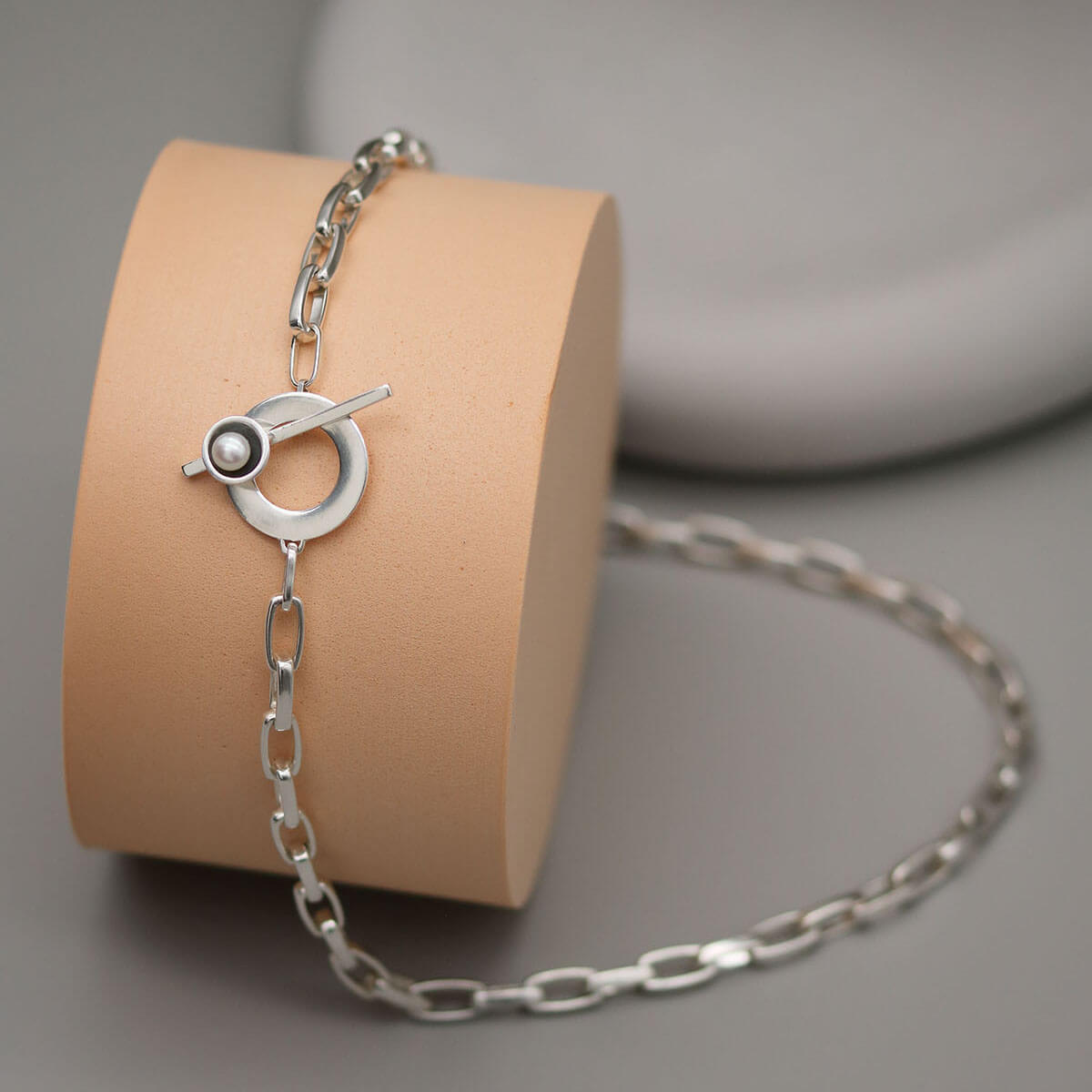 Handmade chunky pearl necklace in sterling silver featuring a bold rectangular trace chain, T-bar toggle clasp and genuine freshwater pearl on a pink display with grey background.
