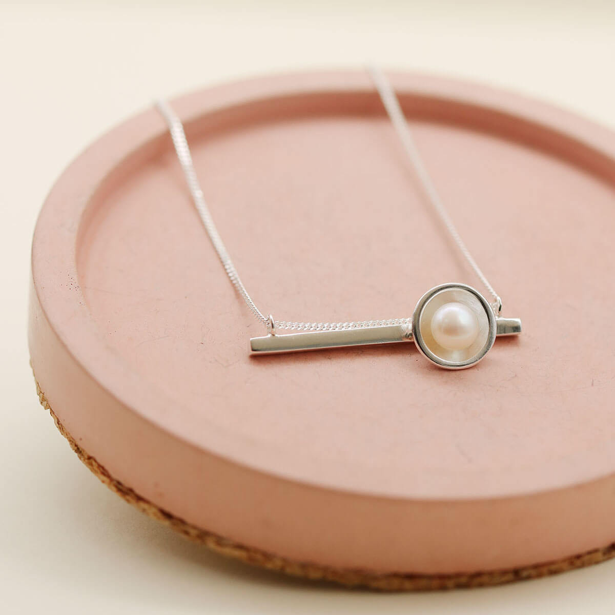 Elegant sterling silver necklace with pearl pendant displayed on a pink ceramic dish, showing the horizontal bar design.