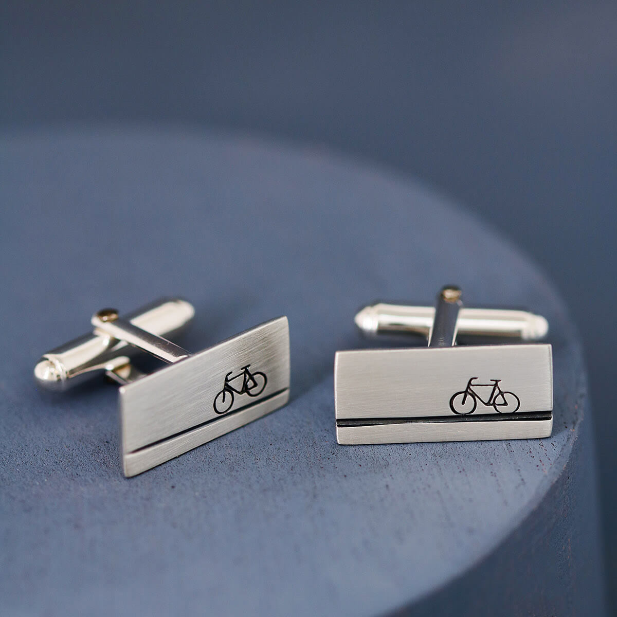 Pair of cycling cufflinks in solid silver on a deep blue background, unique gift for bicycle lovers or thoughtful wedding cufflinks for a sporty groom.