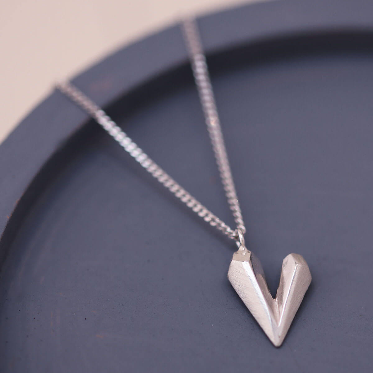 Heart shaped necklace on a blue dish featuring a faceted sterling silver heart charm on an 18 inch chain, a dainty heart necklace gift for her