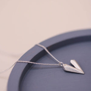 Dainty heart necklace displayed on a blue dish, this heart shaped necklace is handmade in solid sterling silver with a light catching faceted finish