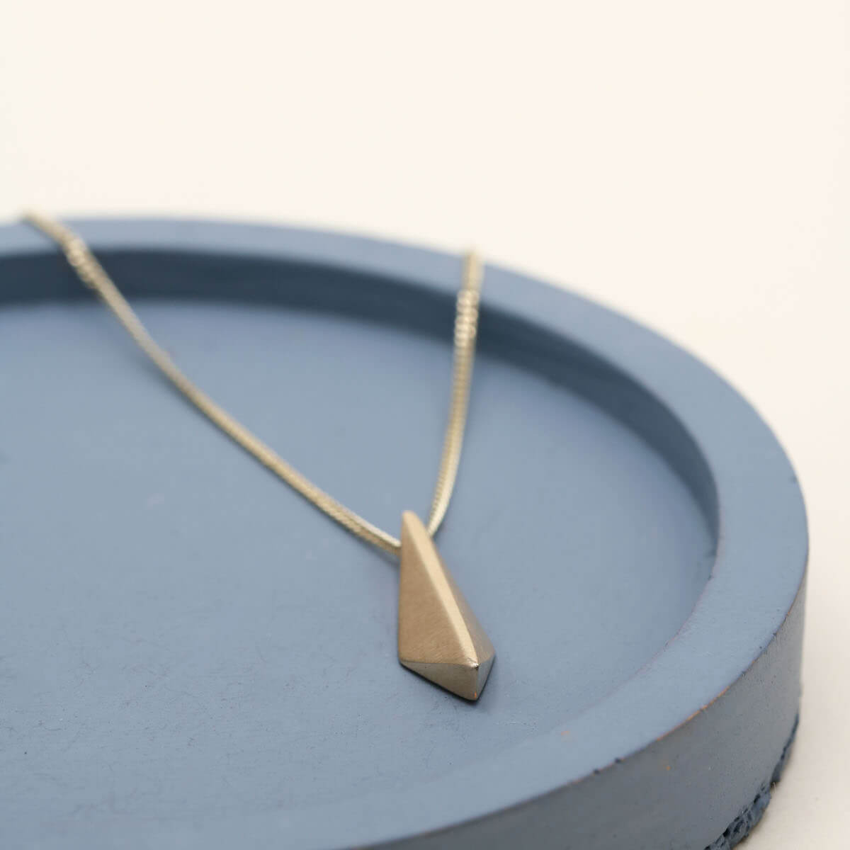 Art Deco-inspired 9ct gold pendant necklace with a geometric kite-shaped pendant on a deep blue dish