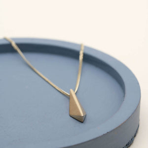 Art Deco-inspired 9ct gold pendant necklace with a geometric kite-shaped pendant on a deep blue dish