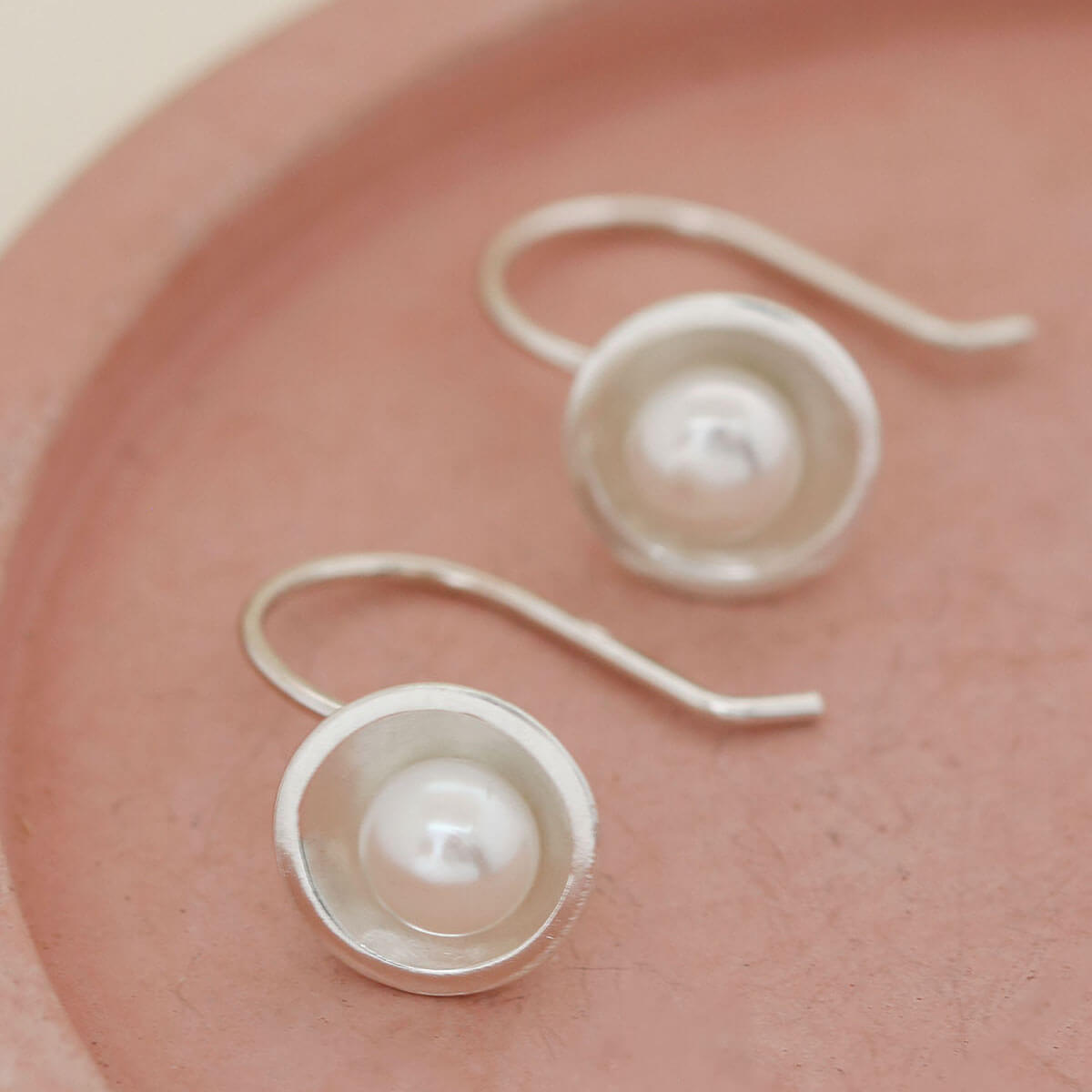 Handmade sterling silver drop freshwater pearl earrings with genuine freshwater pearls displayed on a soft pink ceramic dish.