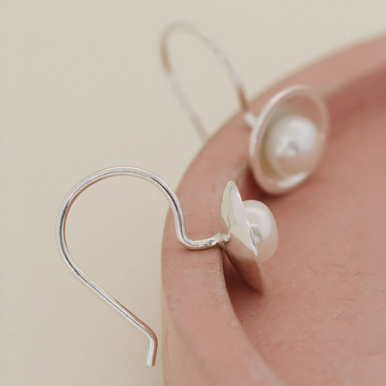 Detail of handmade sterling silver drop earrings with freshwater pearls in polished domed silver settings.