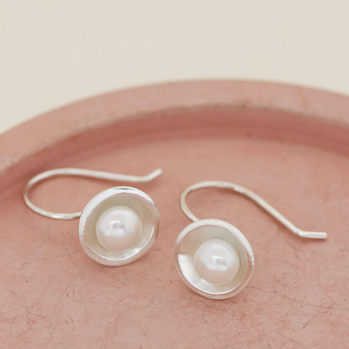 Elegant sterling silver freshwater pearl drop earrings inspired by Art Deco design, photographed on a pink dish.
