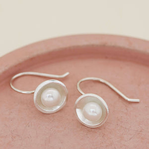 Elegant sterling silver freshwater pearl drop earrings inspired by Art Deco design, photographed on a pink dish.