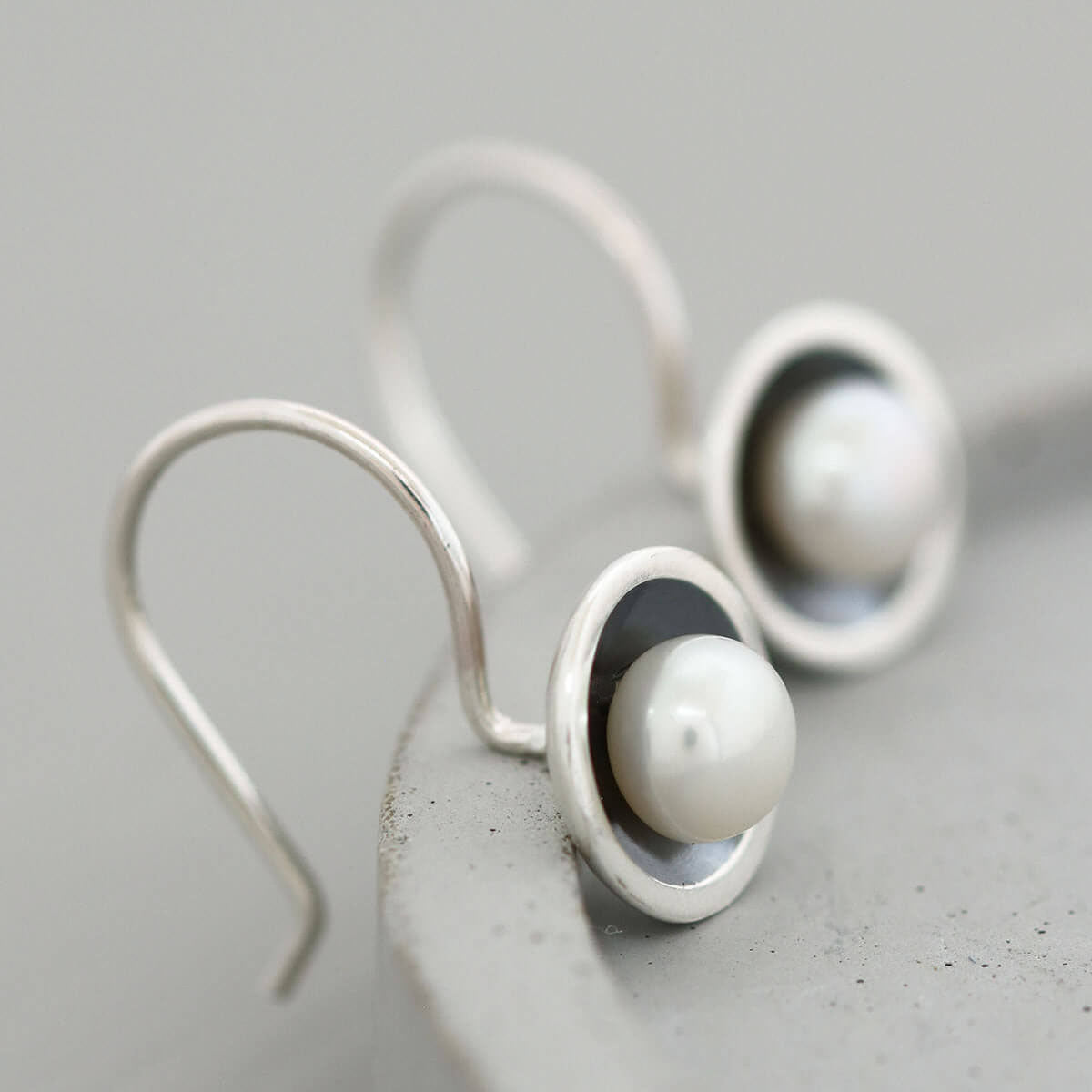 Handmade oxidised sterling silver drop earrings with freshwater pearls photographed on a grey ceramic dish.