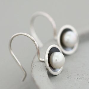 Handmade oxidised sterling silver drop earrings with freshwater pearls photographed on a grey ceramic dish.