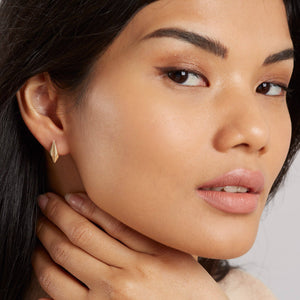 Model styling gold art deco earrings with everyday clothing, subtle geometric gold studs.