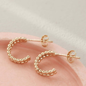 Pair of small 9ct gold hoop earrings photographed on a pale pink dish for an elegant birthday or anniversary gift.