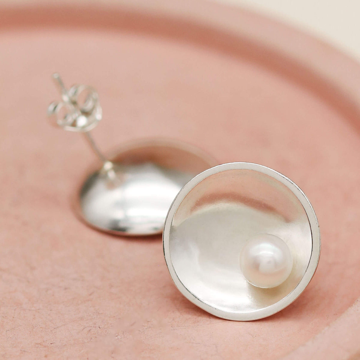 Handmade Signature Sterling Silver Pearl Earrings with genuine freshwater pearls displayed on a soft pink ceramic dish.