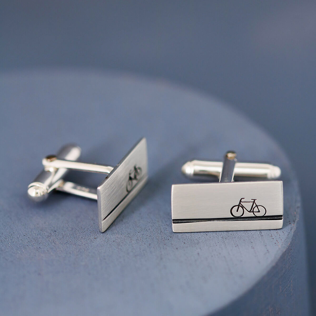 Hand-stamped silver bicycle cufflinks photographed on a deep blue background, perfect birthday gift for cyclists or anniversary gift for him.