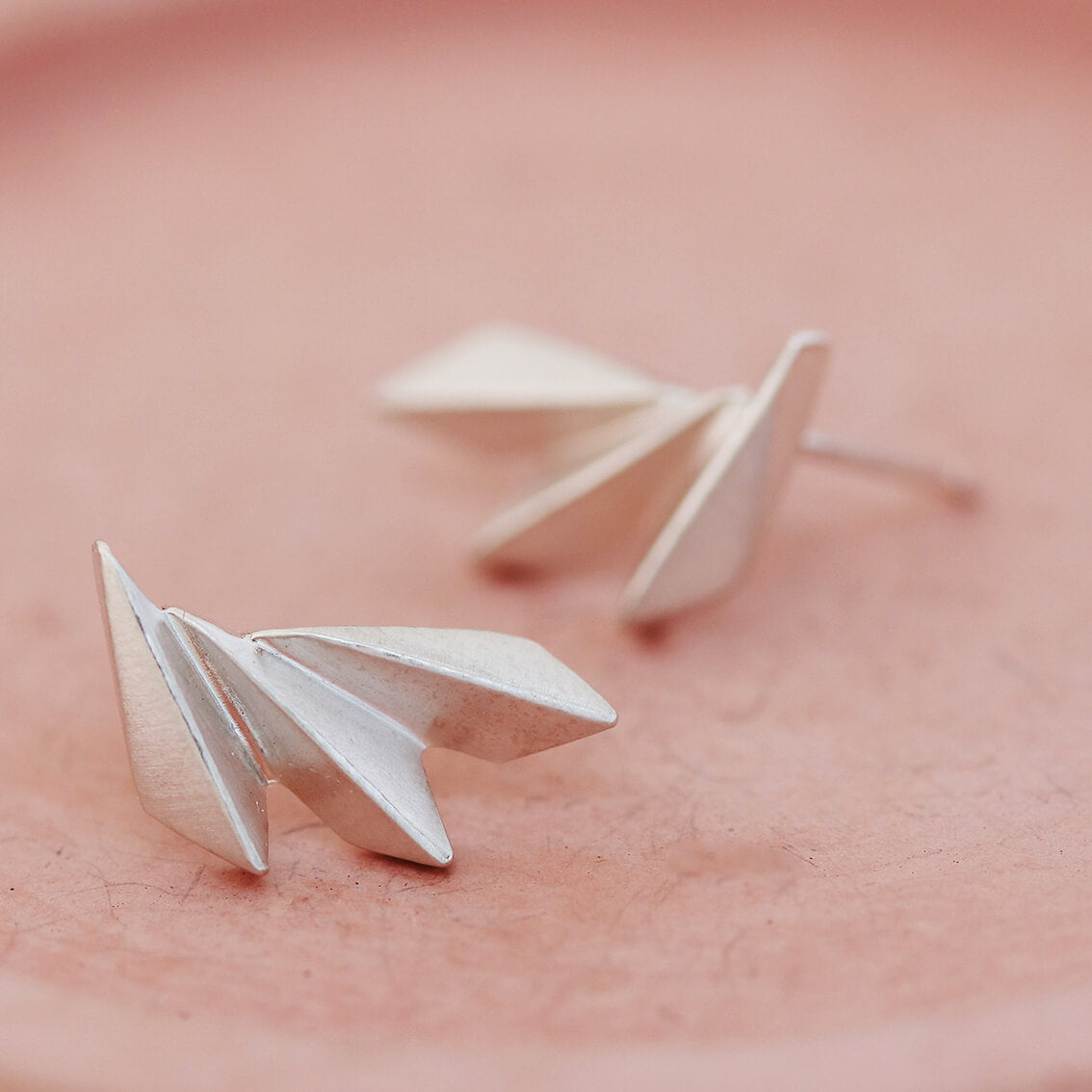 Art deco silver earrings photographed on a pink dish for a detailed view of the texture.