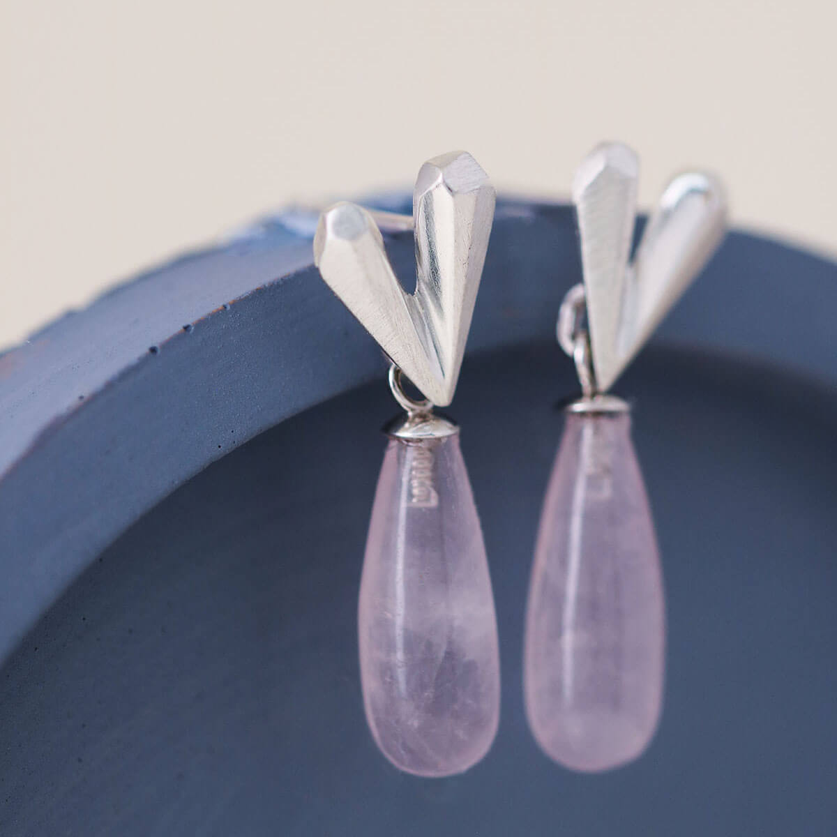 Pink heart earrings featuring a faceted silver heart and teardrop rose quartz gemstone, heart dangle earrings styled on a blue dish
