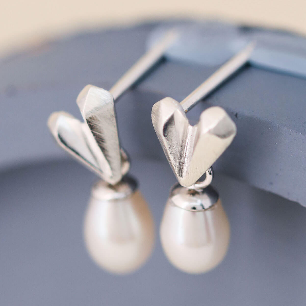 Silver wedding earrings with faceted heart stud and 5x4mm pearl drop resting on a blue dish, delicate heart pearl earrings for bridal jewellery