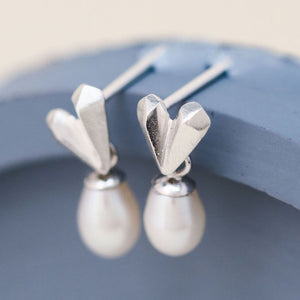 Pair of heart pearl earrings styled on a blue dish showing romantic faceted heart detail and pearl movement, classic silver wedding earrings