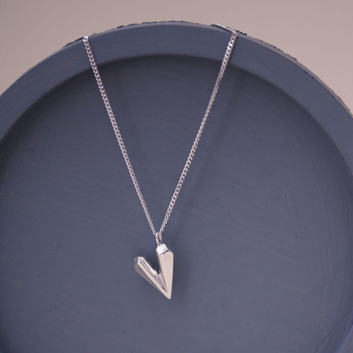 Heart shaped necklace styled on a blue dish, showcasing the handmade faceted silver heart charm on an 18 inch chain