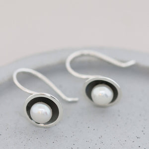 Contemporary hook pearl earrings with genuine freshwater pearls and an oxidised sterling silver finish on a grey dish.