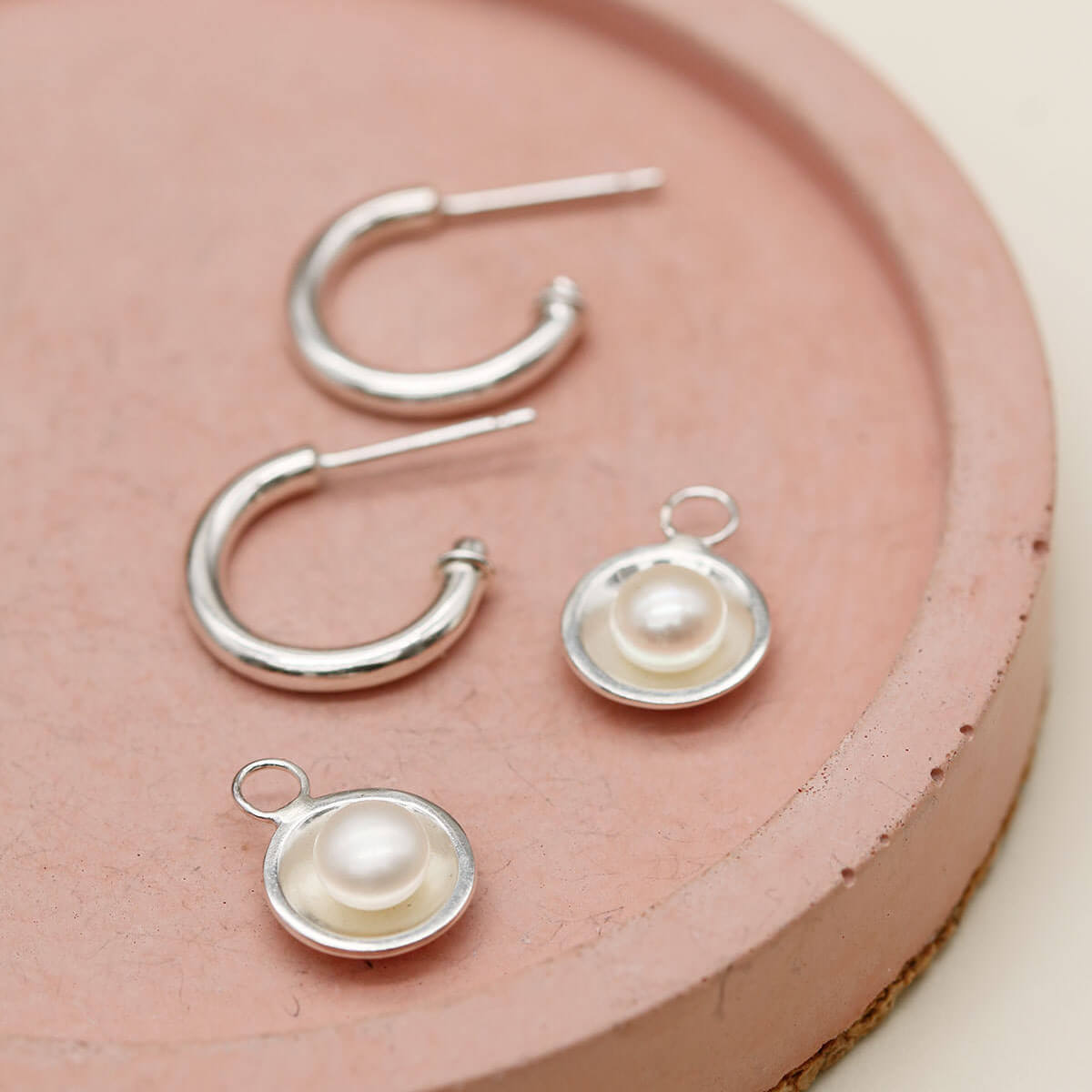 Sterling silver pearl drop hoop earrings handcrafted with genuine freshwater pearls on a pink dish.