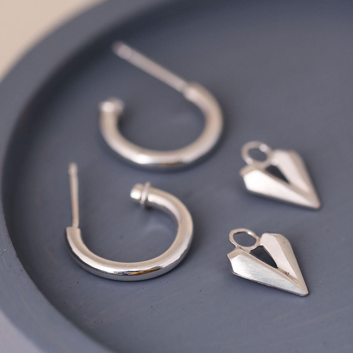 Silver hoop earrings with heart charm on a blue dish, elegant hoops with hearts handmade in sterling silver