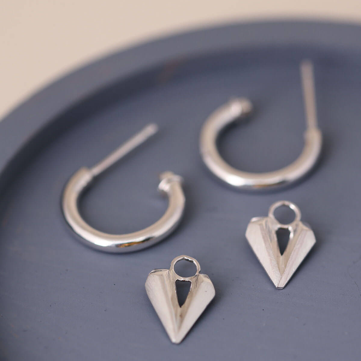 Silver hoop earrings with heart charm photographed on a blue dish, removable heart charm dangling from charm hoops