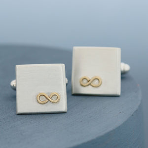 Close-up of one cufflink face on showing the gold infinity symbol, with the second cufflink slightly behind on a deep blue background – Cufflinks personalised and ideal husband anniversary gift.