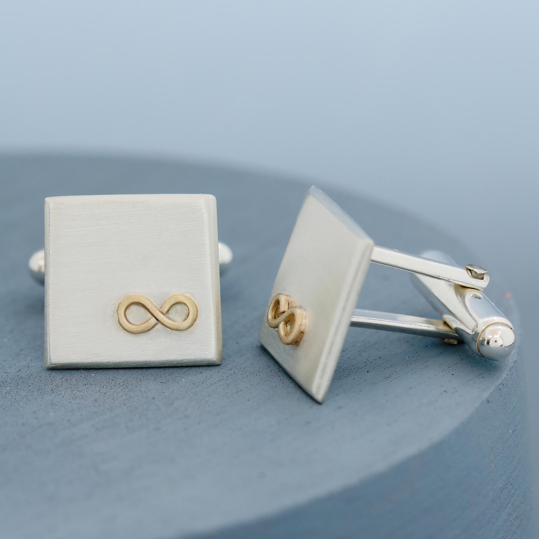 Gold and silver Cufflinks personalised, shown side by side on a deep blue background highlighting the geometric square shape and smooth finish.