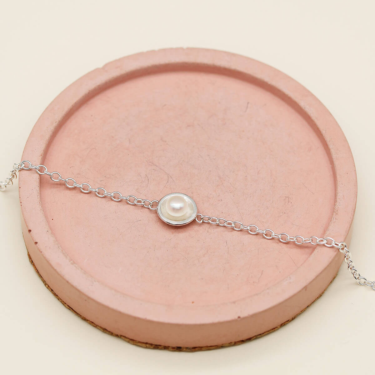 Ladies pearl bracelet handcrafted in solid sterling silver with a genuine freshwater pearl on a pink dish.