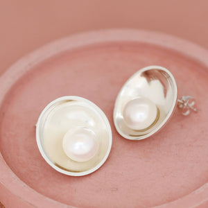 Sterling silver large pearl stud earrings shown on a pink ceramic dish