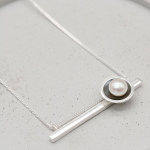 Handmade black geometric pearl necklace highlighting the hidden chain design and freshwater pearl detail.