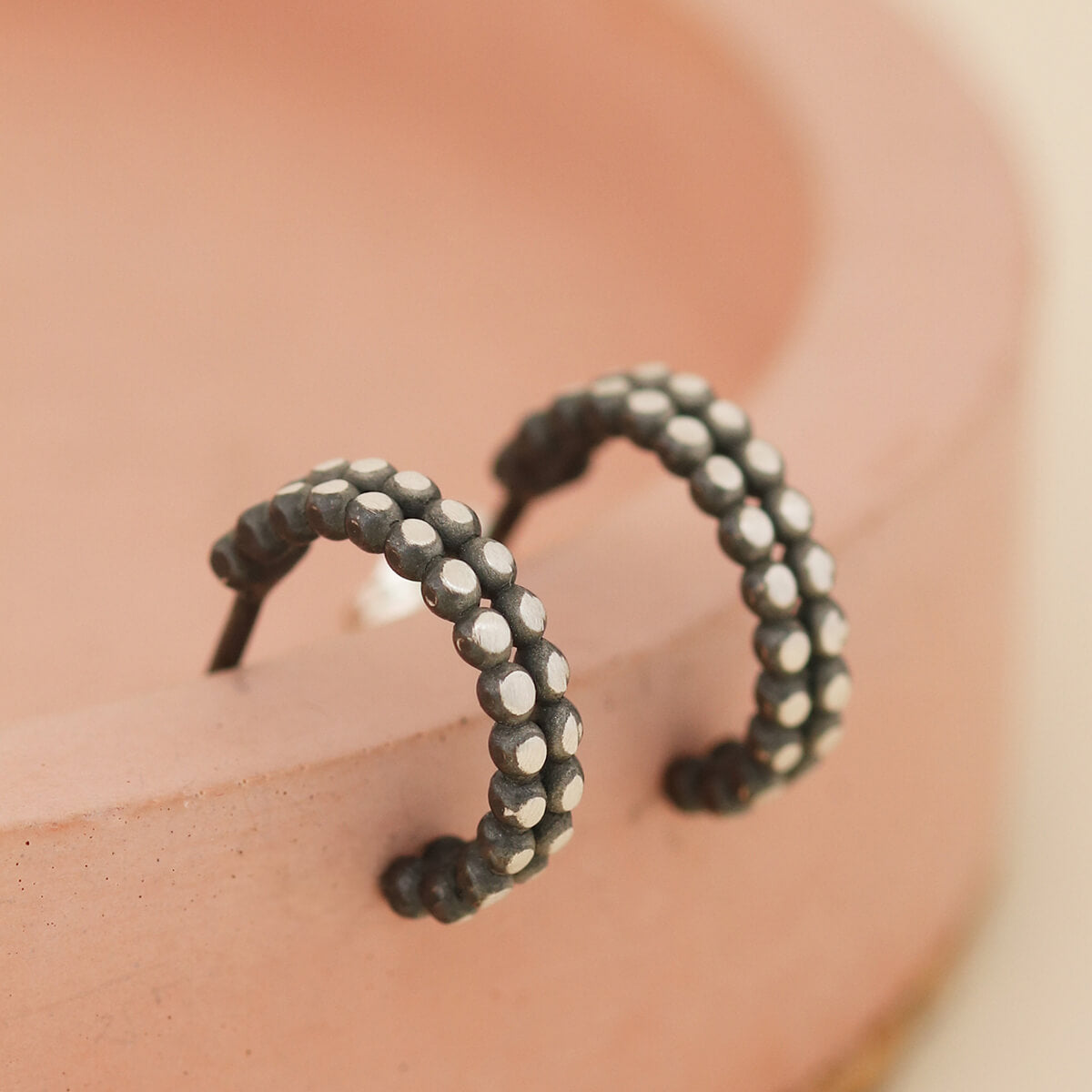 Little black hoop earrings with silver detailing shown on a pink dish, minimalist huggie hoops